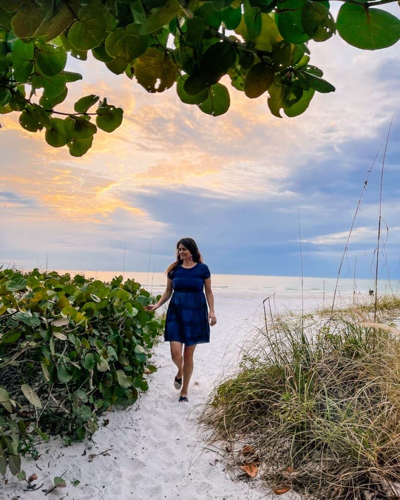 girl in navy blue dress walking back from the beach at sunset on a greenery lined bath
