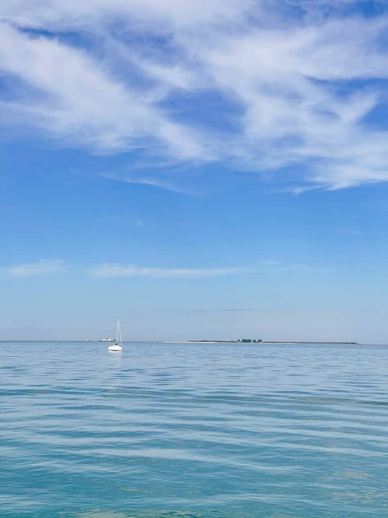 White sail boat in the distance on calm blue waters with a pure blue sky and fluffy white clouds in the sky
