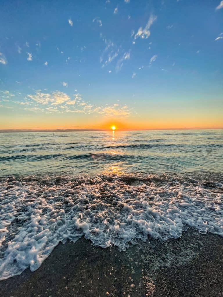 beautiful blue sky with an orange and gold sun setting on the horizon over the blue waters of the gulf of mexico