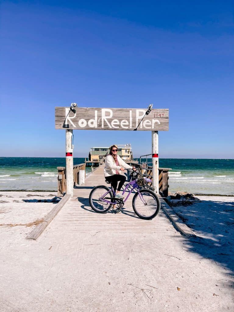 girl on purple bike posing in front of Rod & Reel Pier with ocean backdrop