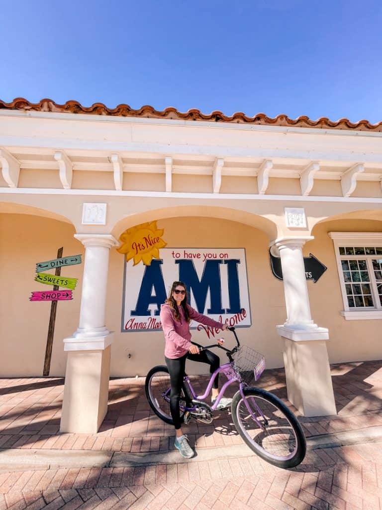 girl on purple bike posting in front of "welcome to AMI" sign